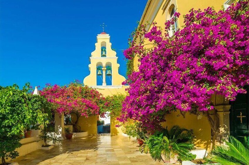 A yellow building with a bell tower, surrounded by bougainvillea flowers. 5