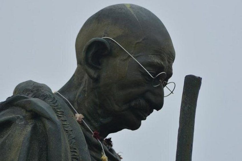 A statue of a man with a bald head, wearing glasses, and holding a staff. 5