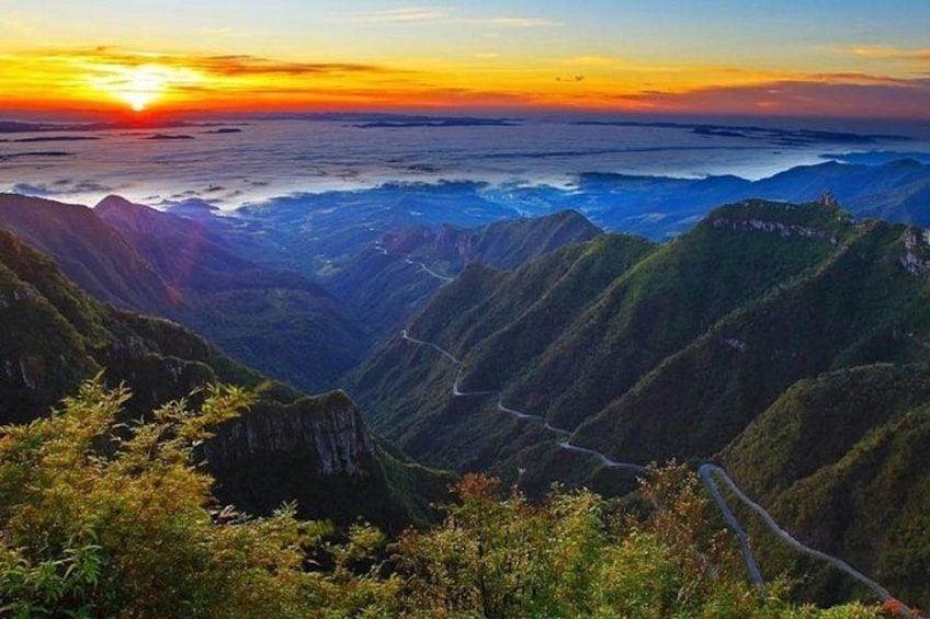 A mountainous landscape with a winding road and a sunset. 1