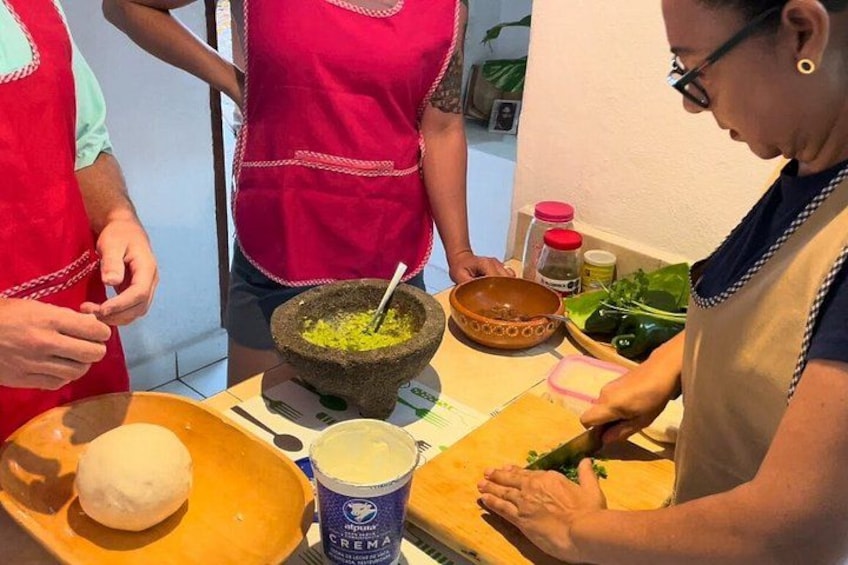 A person preparing food, with a bowl of green mixture, a bowl of white substance, and a container of crema. 4