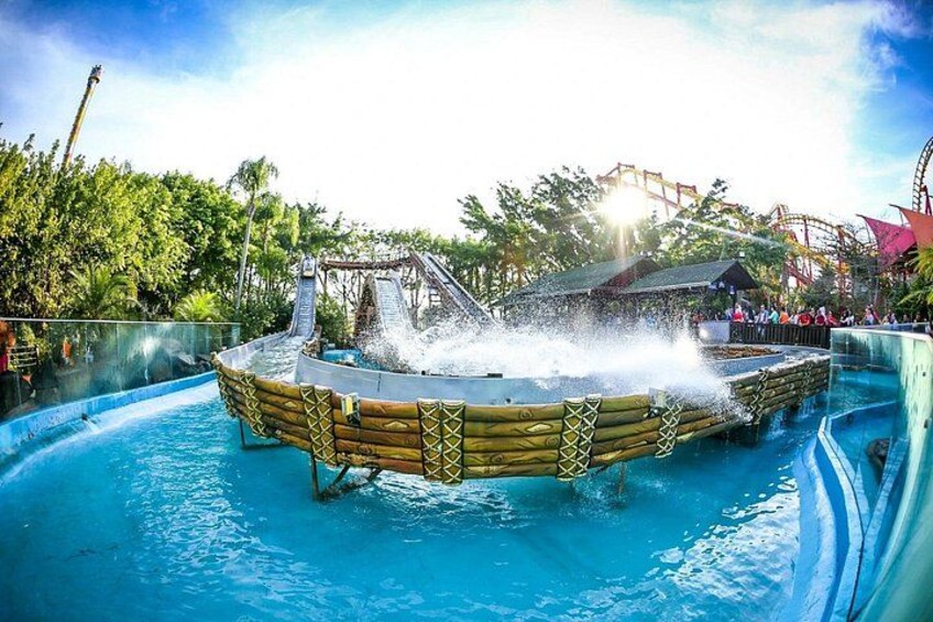 A water ride with a wooden boat structure, a water slide, and a roller coaster in the background. 5