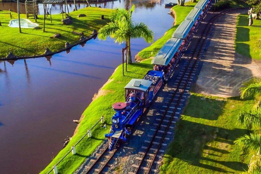 A model train on tracks with a water body and greenery. 2