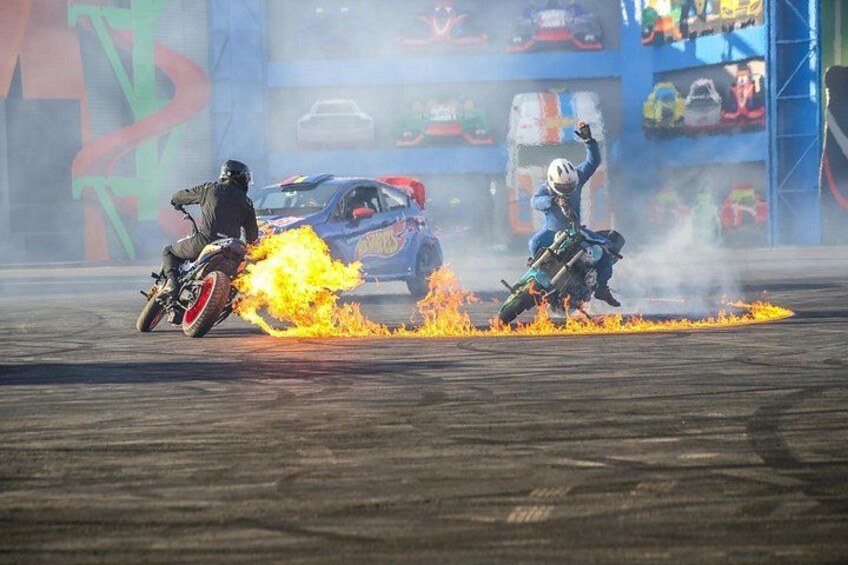 Two motorcyclists performing stunts with flames on a track. 4