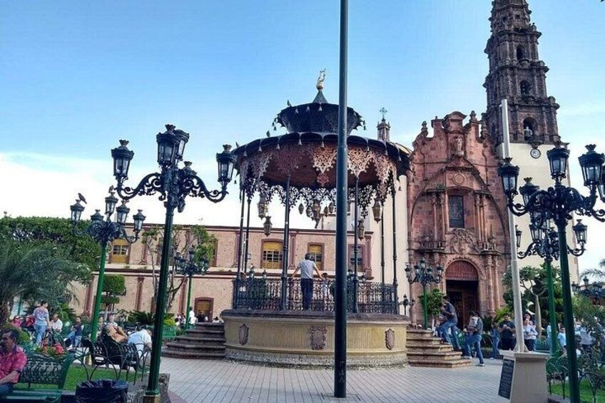 Une place agrémentée d’une fontaine centrale, de réverbères décoratifs et d’un bâtiment historique doté d’un clocher. 1