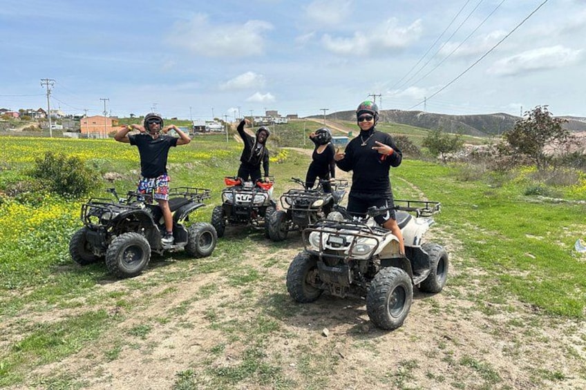 Four people on ATVs in a grassy field with hills in the background. 4