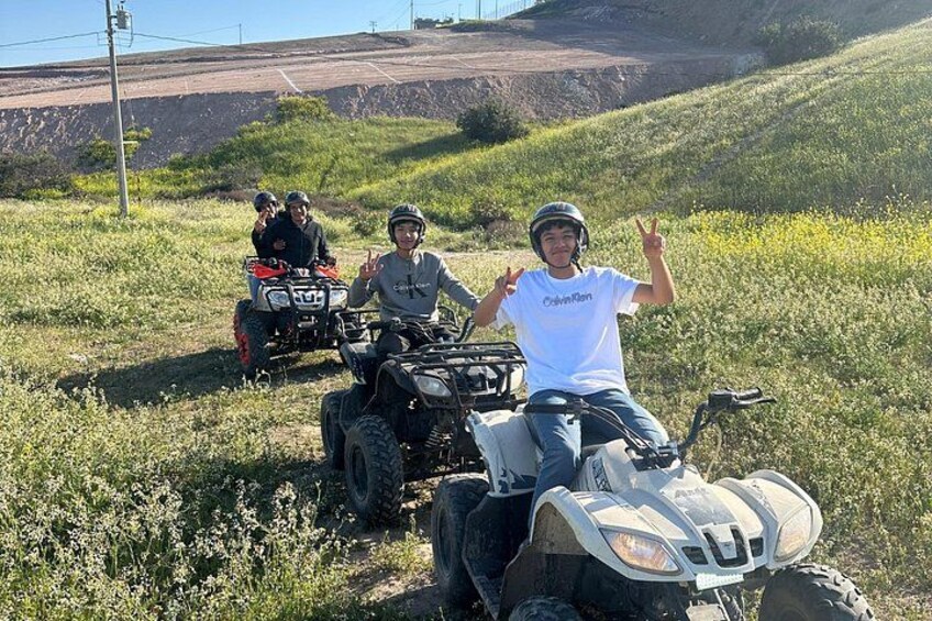 Three people on ATVs in a grassy field with hills in the background. 5