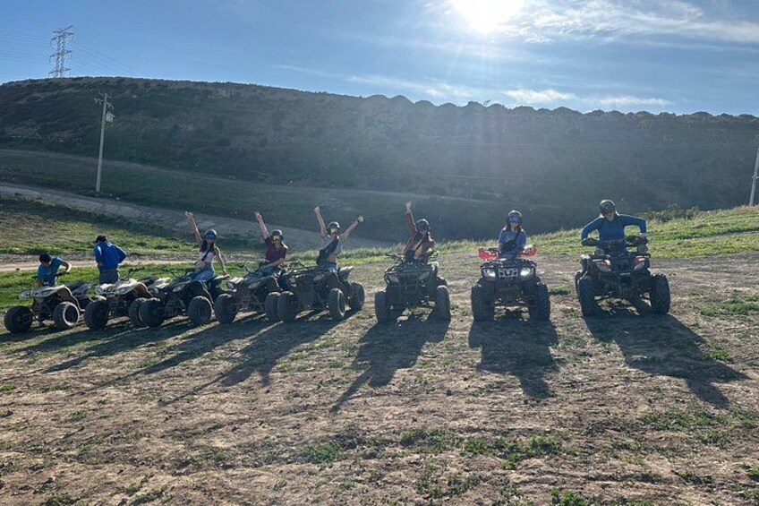A group of people on quad bikes in a grassy field with a hill in the background. 1