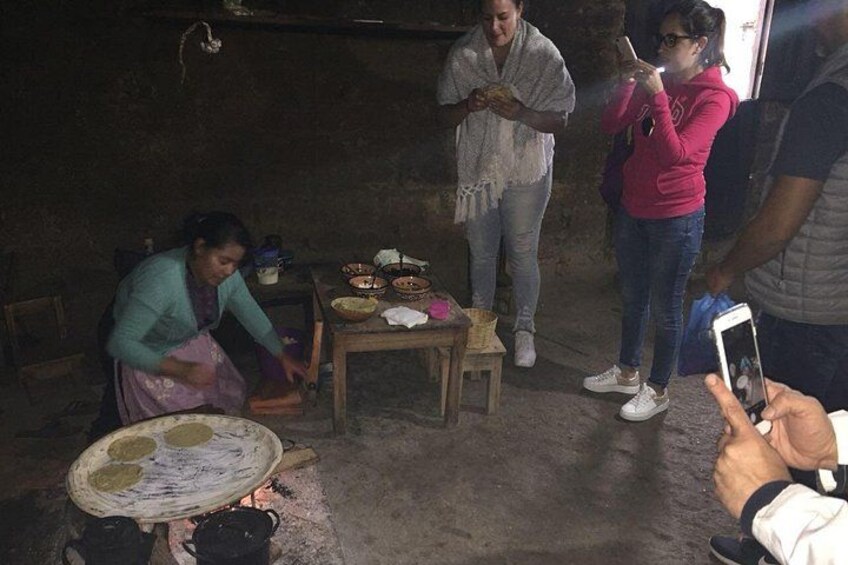 Una mujer cocina con una olla en la estufa, una mesa con cuencos y una persona tomando una foto. 4