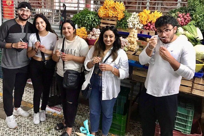 Un groupe de personnes se tient dans un marché où sont exposés divers fruits et légumes. 1