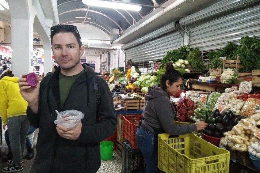 Une personne tenant un fruit violet, une autre personne choisissant des légumes, et divers produits frais exposés sur un marché. 3