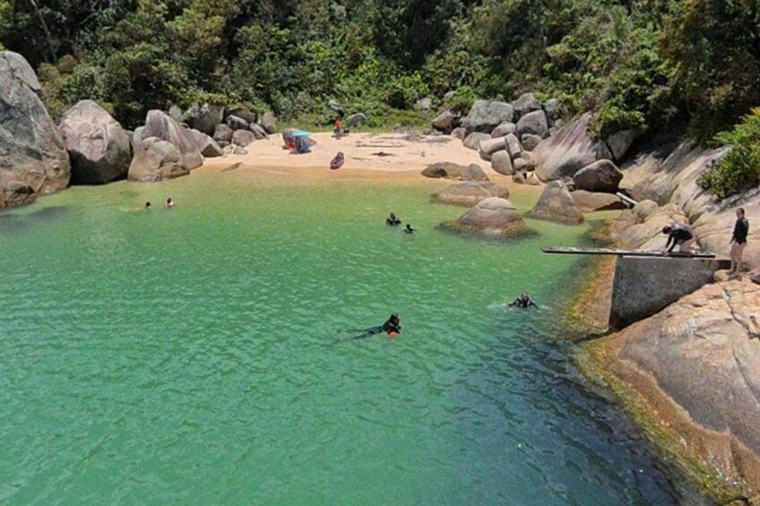 Una piscina turquesa cristalina rodeada de rocas, con gente nadando y una zona de playa al fondo. 2