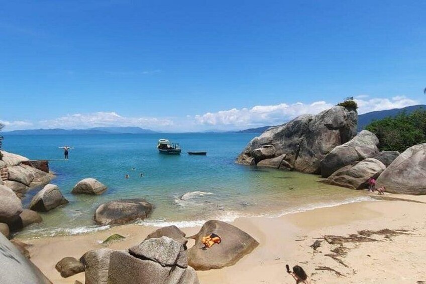 Una playa con grandes rocas, agua azul cristalina y un barco a lo lejos. 3