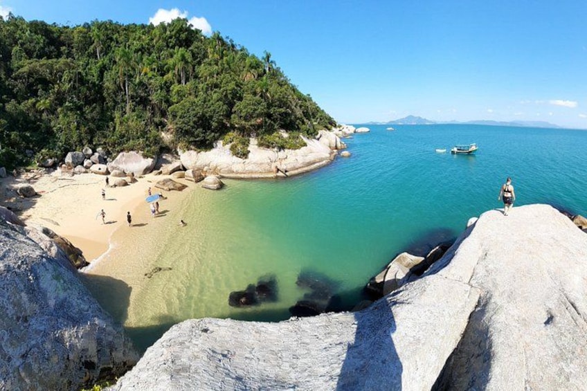 Una playa con agua turquesa cristalina, costa rocosa y una persona caminando por la arena. 1
