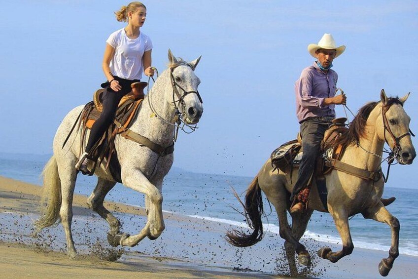 Deux personnes à cheval sur une plage, avec l’océan en arrière-plan. 1