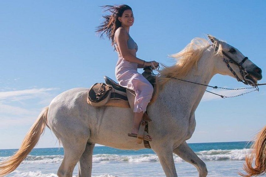 Una persona cavalca un cavallo bianco su una spiaggia, con le onde sullo sfondo. 4
