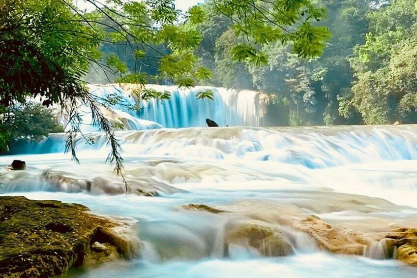 A waterfall cascading over rocks, surrounded by lush greenery. 1