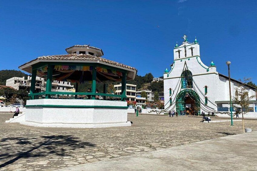 A gazebo with a tiled roof, a white church with a green archway, and a clear blue sky. 5