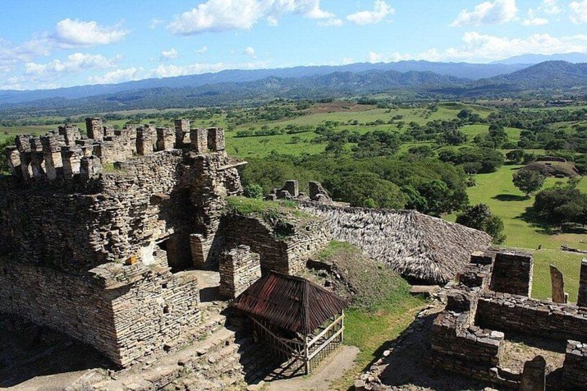 A historical stone castle with ruins, surrounded by lush green fields and distant mountains. 2