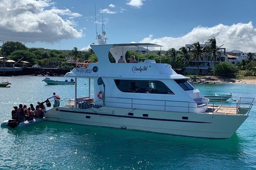 Un yacht blanc baptisé « CandySail », avec des personnes à bord, est amarré dans une marina. On aperçoit une plage et des palmiers en arrière-plan. 1