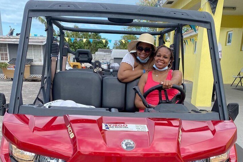 A red utility vehicle with two people inside, one driving and one sitting in the passenger seat. 2