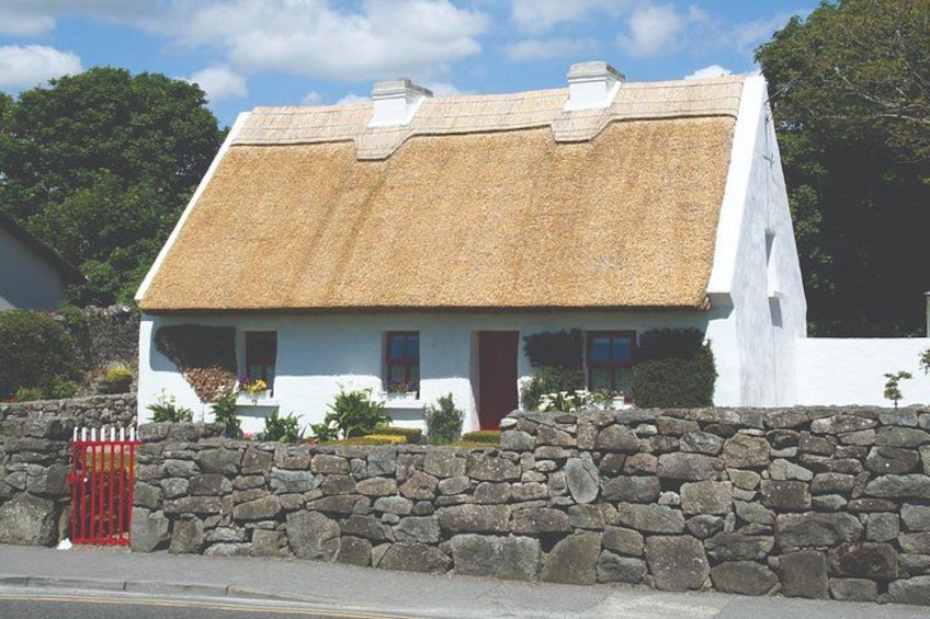 Una casa blanca con techo de paja, muro de piedra y una puerta roja. 2
