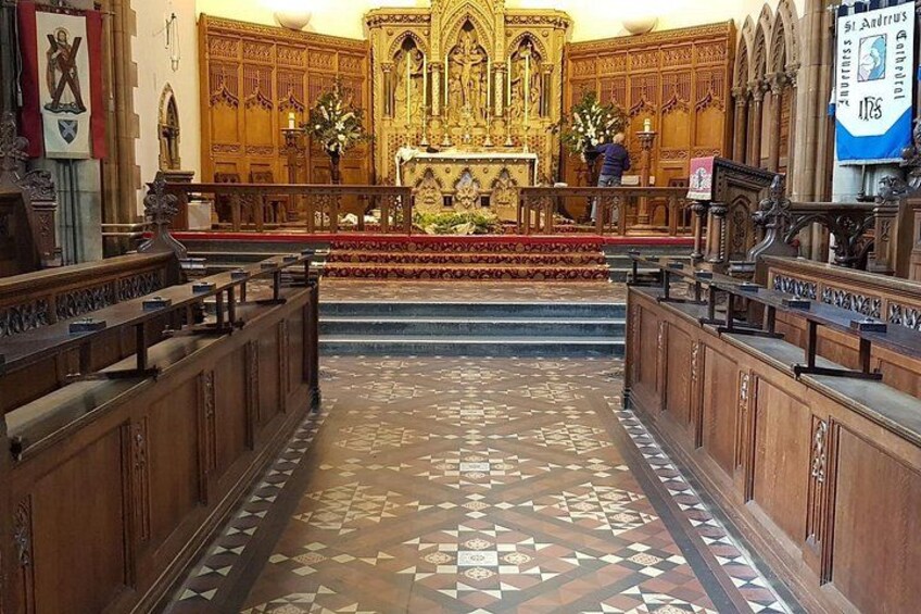 An ornate church interior with a central altar, pews, and a patterned floor. 2