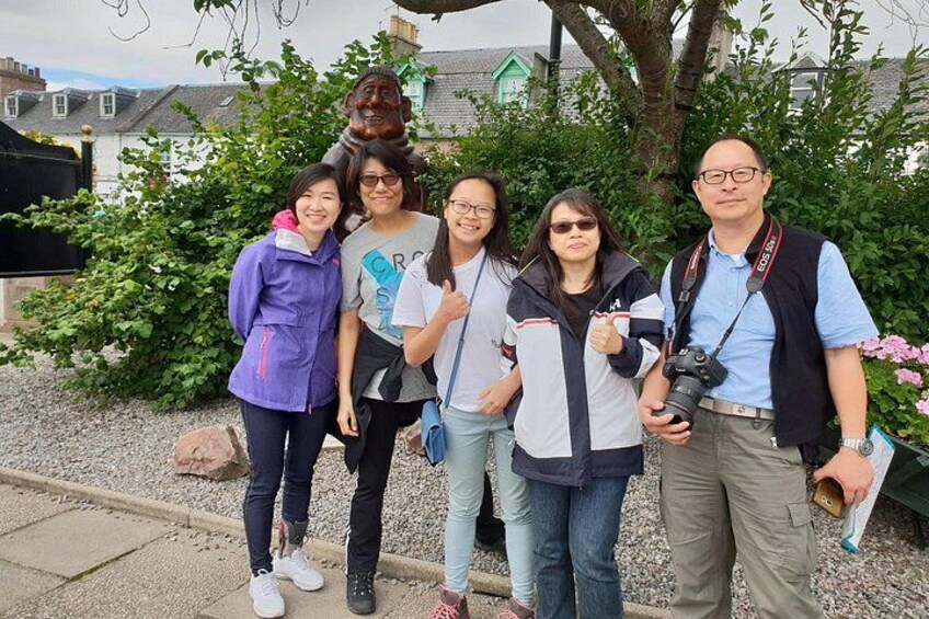 A group of people standing outdoors with a statue and greenery in the background. 3