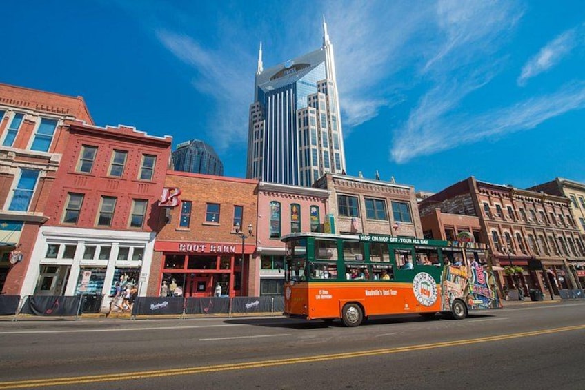 A city street with a green and orange bus, buildings, and a tall skyscraper. 5