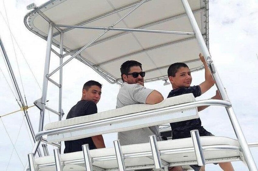 Three people on a boat deck with metal railings and a canopy overhead. 2