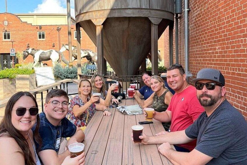 A group of people sitting at an outdoor wooden table, enjoying drinks and conversation. 3