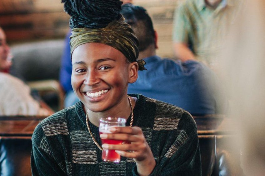 A person sitting at a table in a restaurant, holding a glass of red beverage. 4