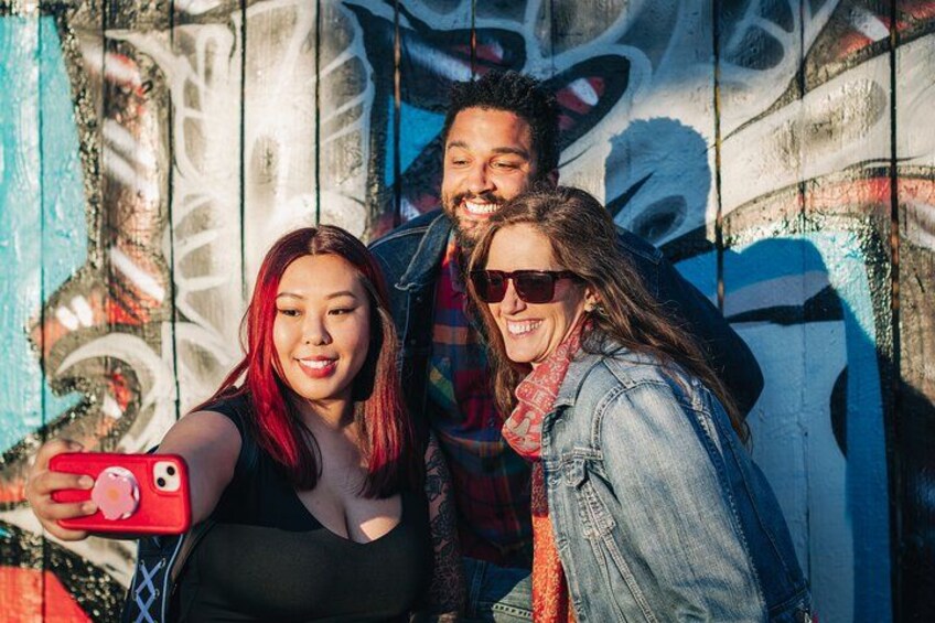 Drei Personen machen ein Selfie mit Graffiti im Hintergrund. 5