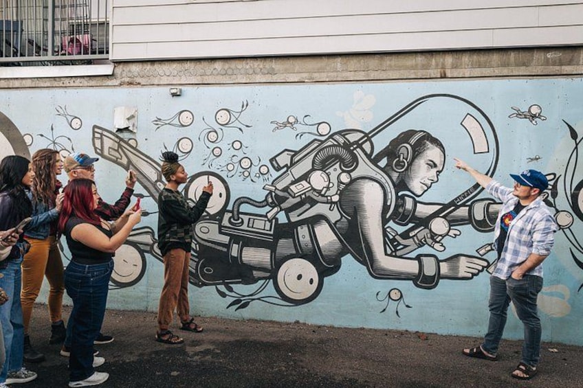 A mural of a woman in a spacesuit on a wall, with a group of people observing it. 3