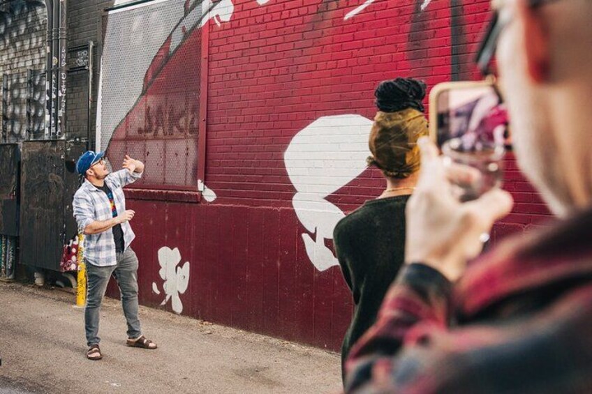 Eine Person fotografiert ein Wandgemälde an einer roten Wand. 4