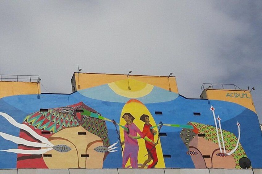 A colorful mural on a building with abstract figures and patterns. 1