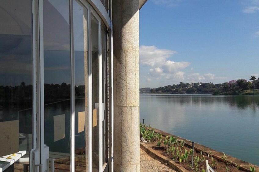 A lakeside view with a glass building, a concrete pillar, and a row of plants. 2