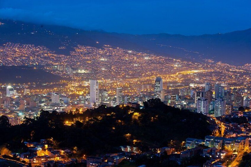 Un paisaje urbano nocturno con edificios iluminados y una montaña al fondo. 3