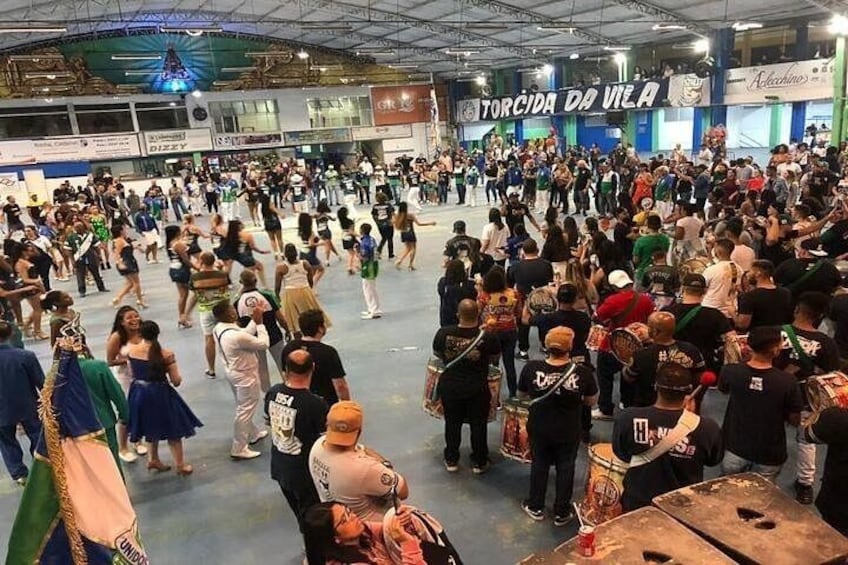 A crowded indoor event with people dancing and a banner reading 'TORCIDA DA VELA'. 3
