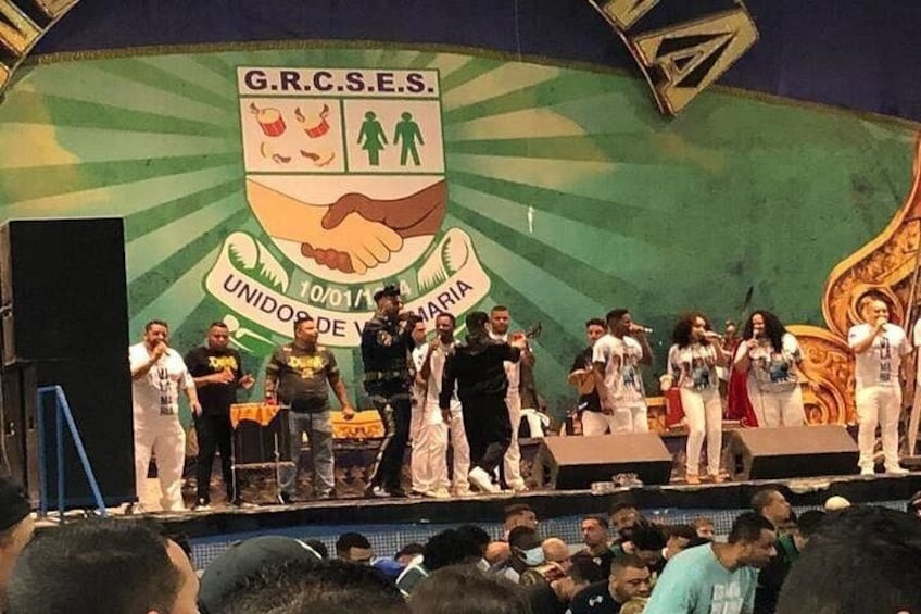 A stage with a group of people, a banner with G.R.C.S.E.S. and a handshake symbol, and a crowd in front. 2