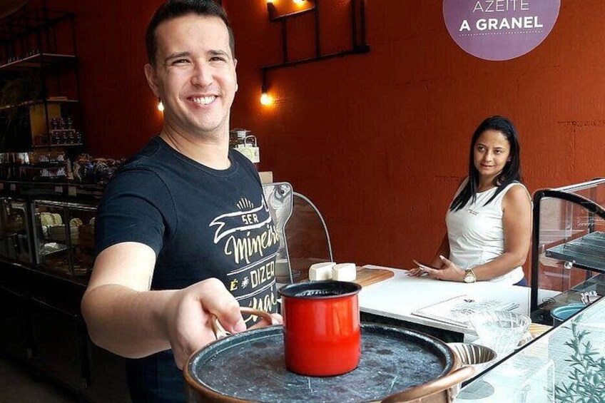 A person holding a red mug, a woman standing behind, and a menu on the table. 2