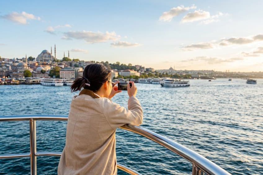 Eine Person fotografiert eine Skyline mit einer markanten Moschee und Booten auf dem Wasser. 2