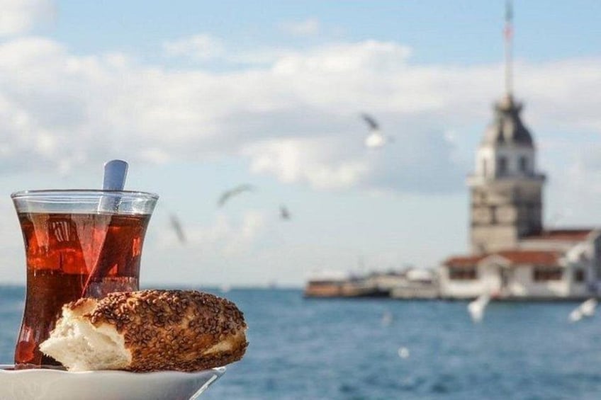 A glass of tea, a piece of bread, and a distant view of a tower by the sea. 1
