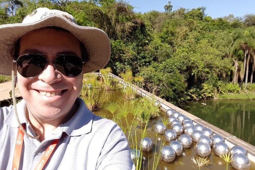 Una persona con sombrero y gafas de sol, un muelle de madera y un estanque con nenúfares. 4