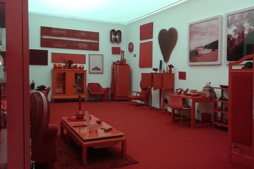 Un salón con decoración roja, que incluye un aparador de madera, un sillón rojo y una mesa con libros. 3