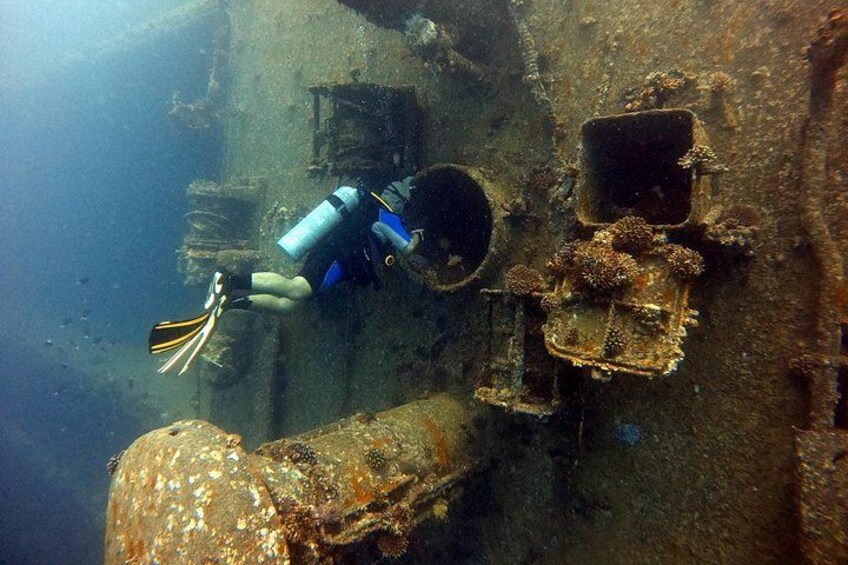 A diver exploring an underwater wreck with rusted metal structures and marine growth. 2