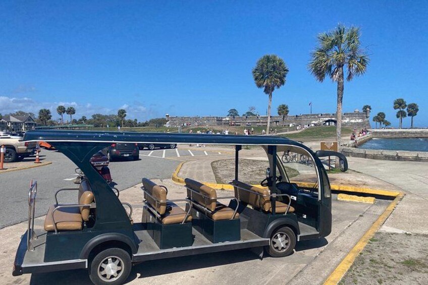 A golf cart parked in a parking lot with palm trees and a clear blue sky in the background. 2
