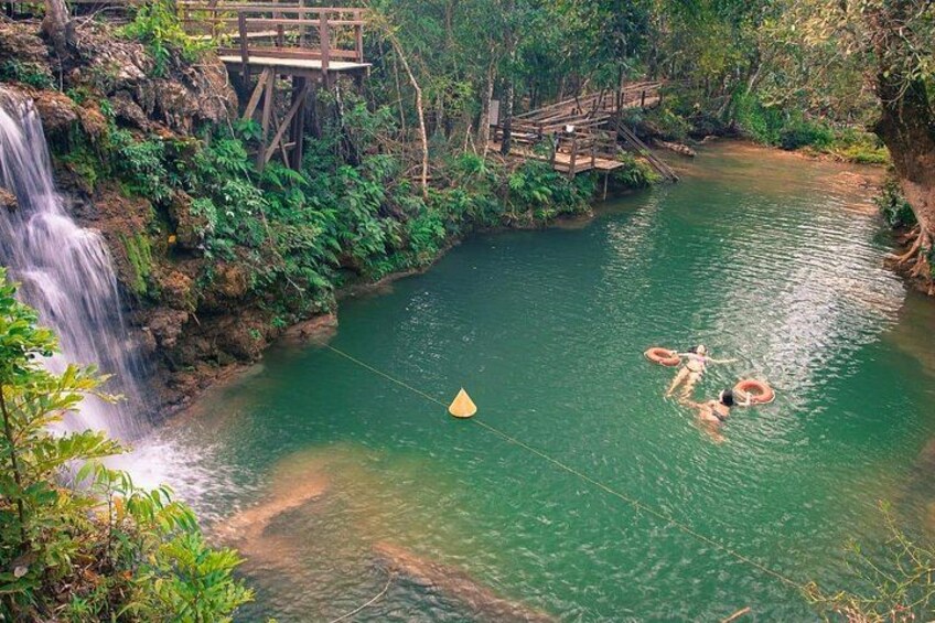 A waterfall, a wooden bridge, and people swimming in a river. 4