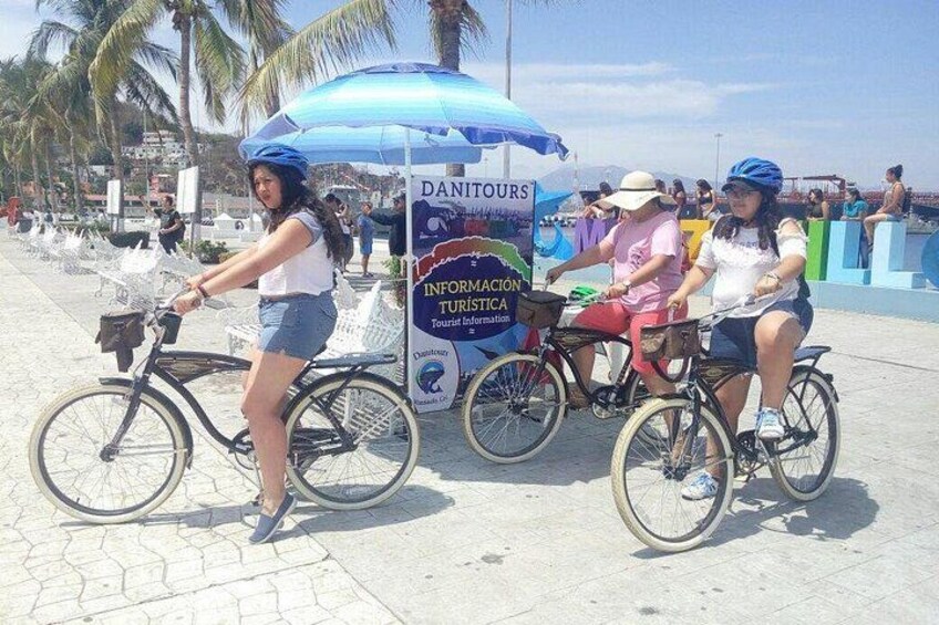 Three people on bicycles near a blue umbrella and a sign that reads 'DANITOURS.' 2