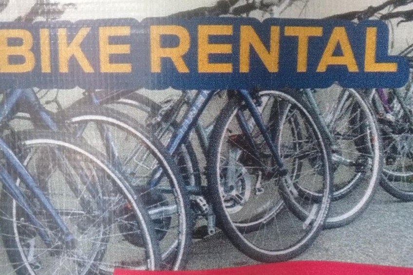A bike rental sign with bicycles parked in the background. 5