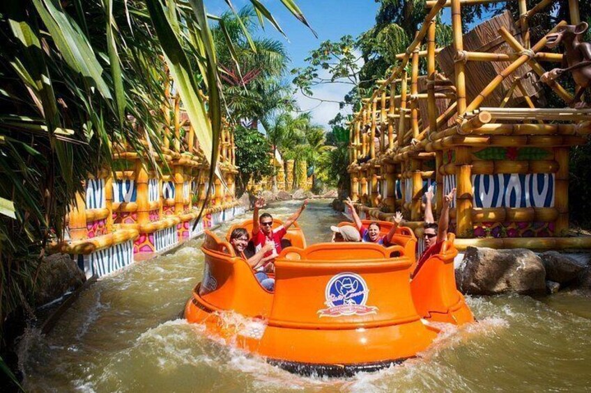 Een waterattractie met oranje boten, omgeven door bamboestructuren en tropische begroeiing. 5